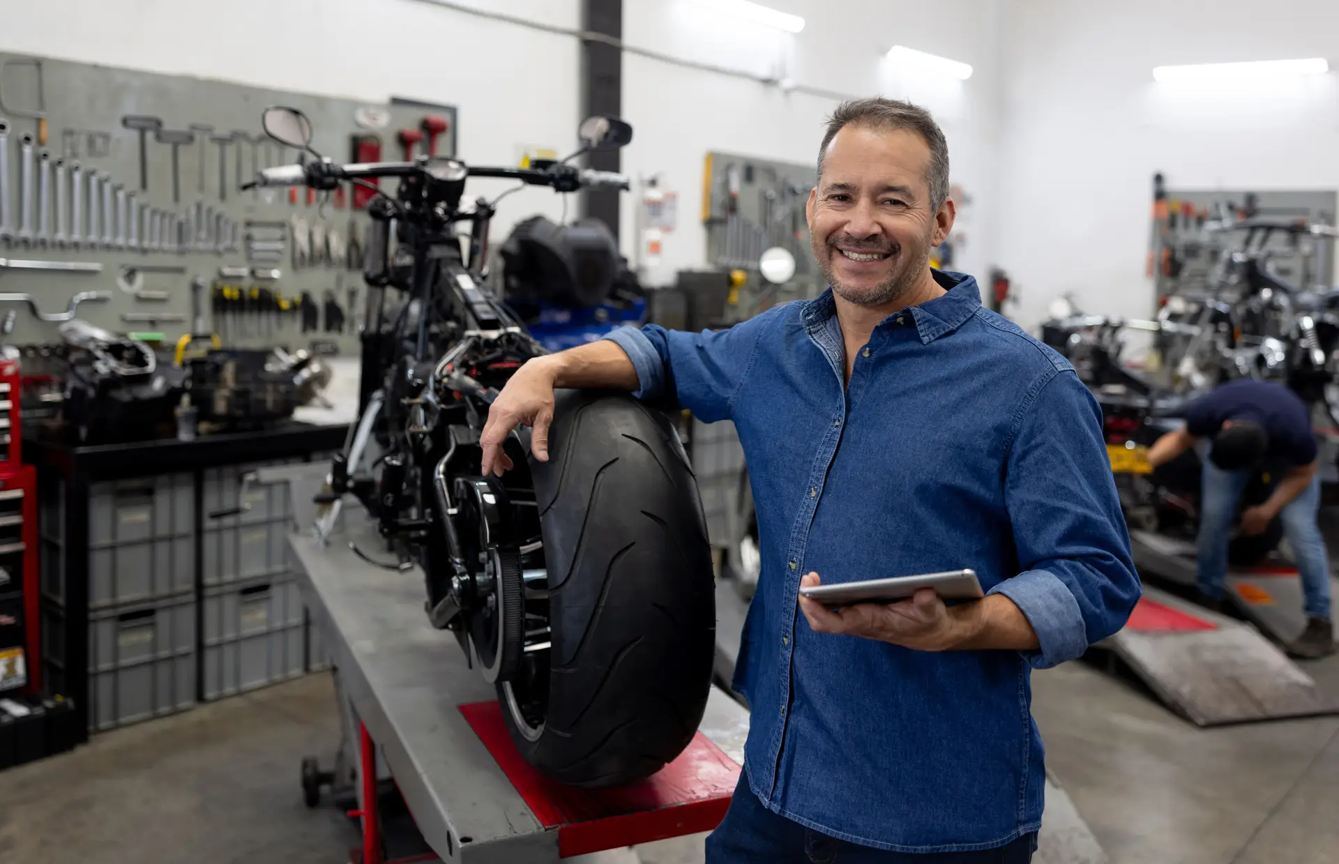 Portrait of a Latin American business owner smiling at a motorcycle repair shop and using a digital tablet